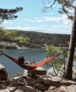 A girl relaxing in a red galmping hammock while watching the lake.