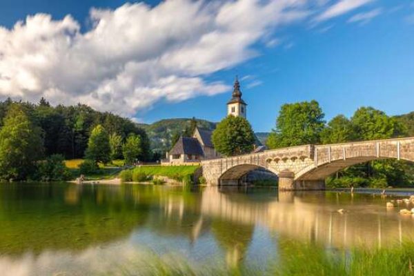 Landscape of Lake Bohinj in the summertime under a clear sky. View of a church and stone bridge in the background. Slovenia.